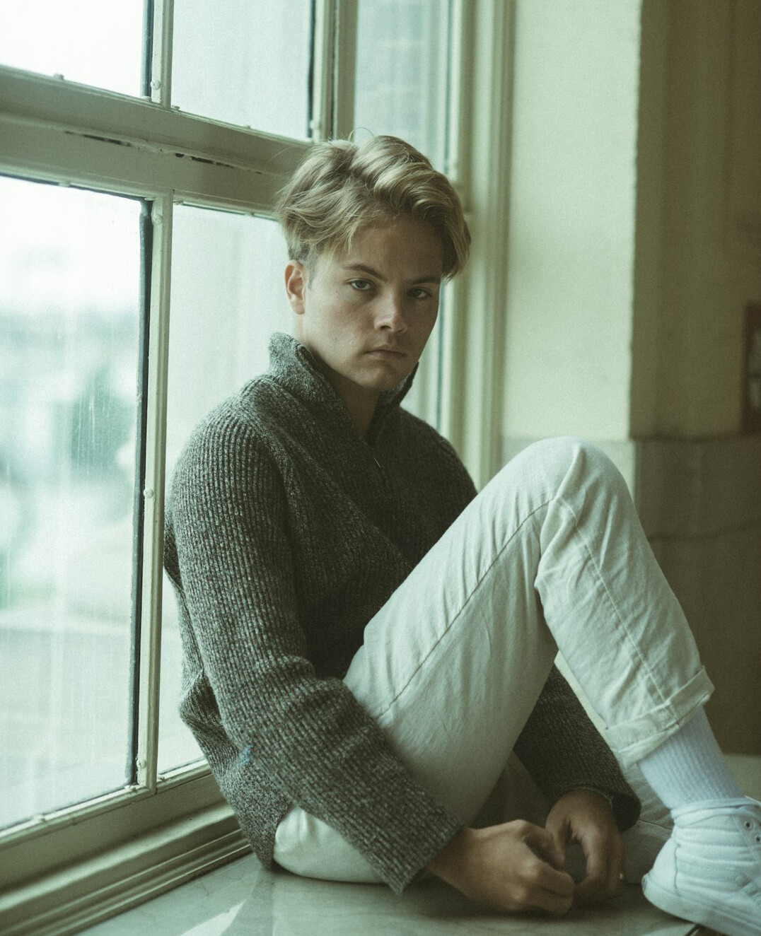 Portrait of a young man with blond hair in a gray sweater